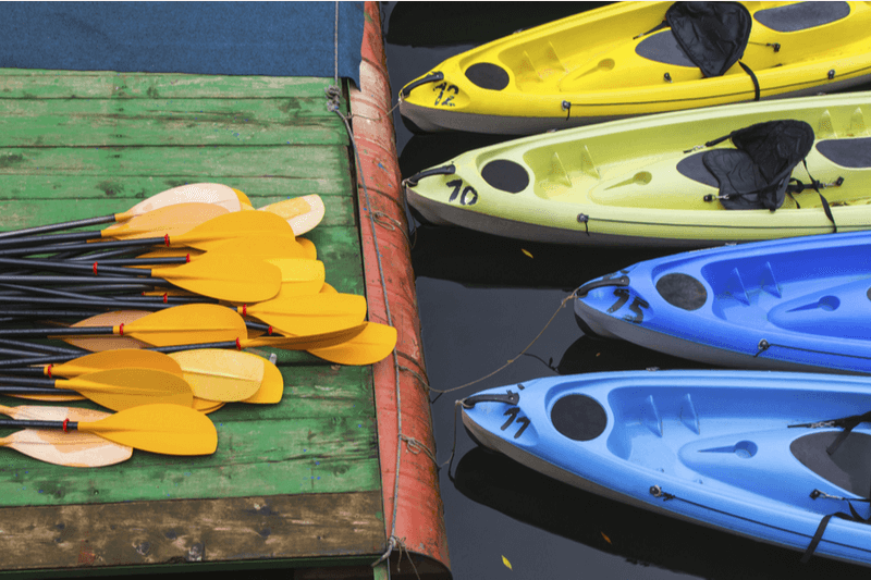 Four kayaks rest at the dock with a pile of paddles.