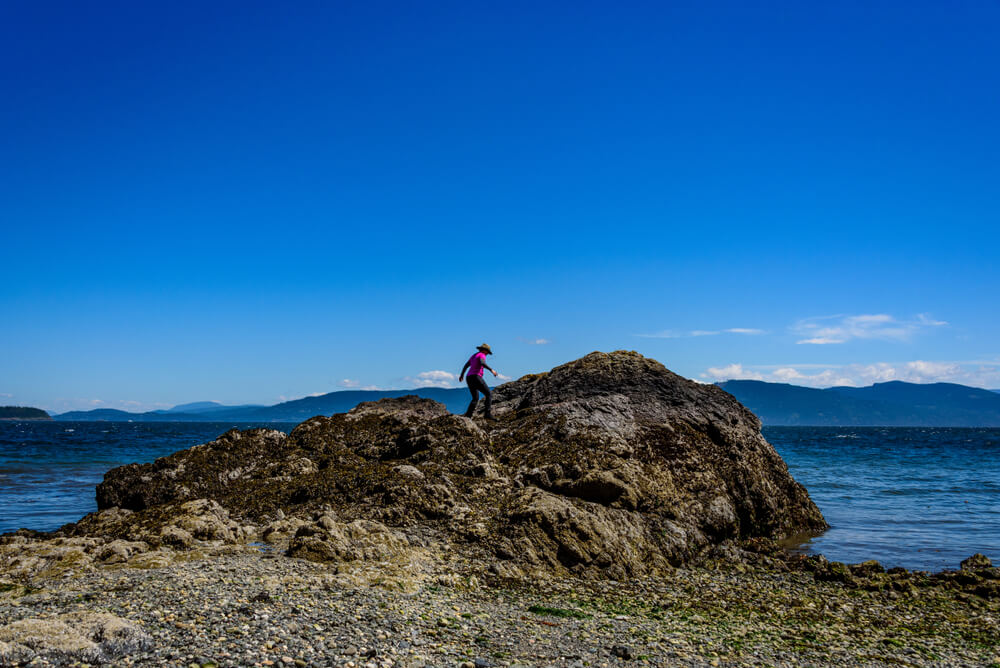 An avid hiker scales a massive rock amid the San Juan Islands